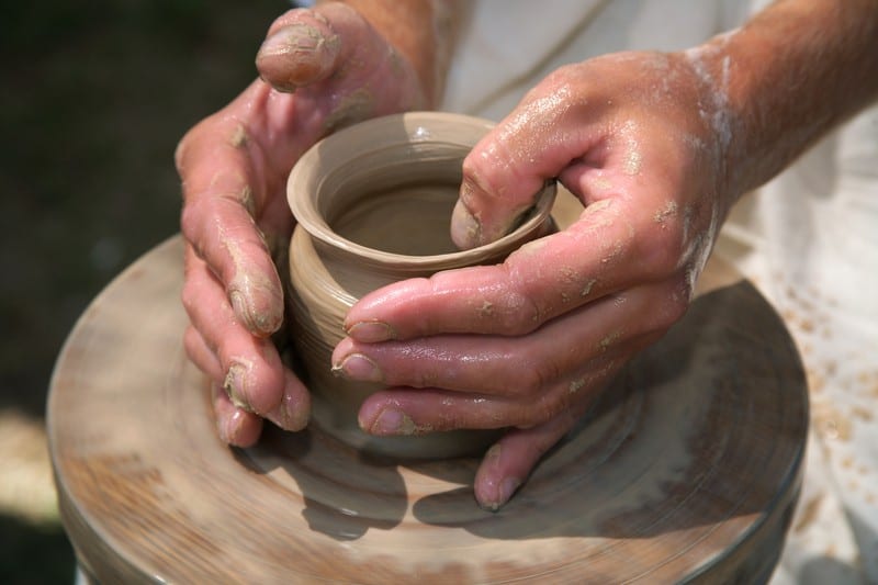 two hands molding clay on potter's wheel