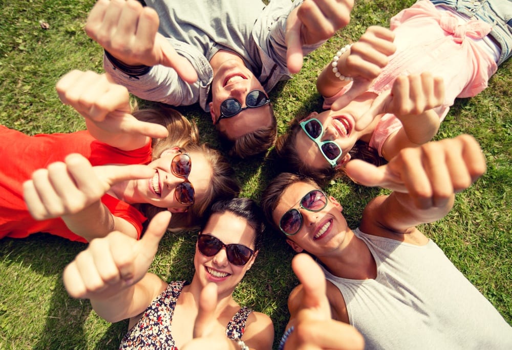 young friends posing for picture laying on ground in circle with thumbs up